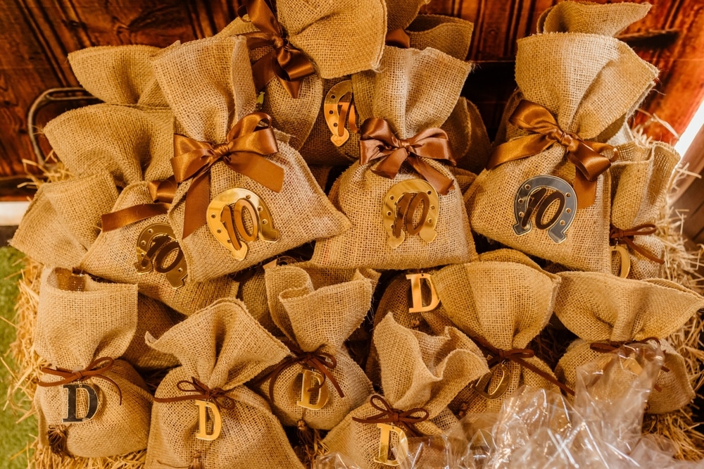 Burlap gift bags with brown ribbons and decorative metal letters and horseshoes, arranged on a hay bale