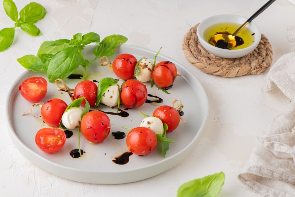 Caprese skewers with tomatoes, mozzarella balls, basil and spices on white table