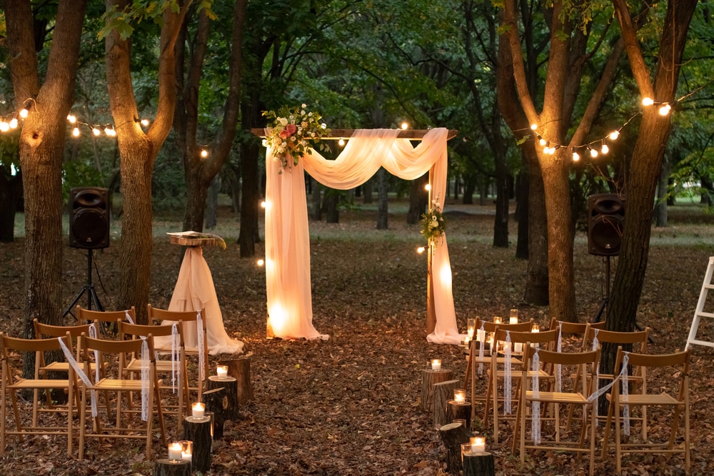 Seats for guests at a beautiful wedding with light bulbs in the forest.