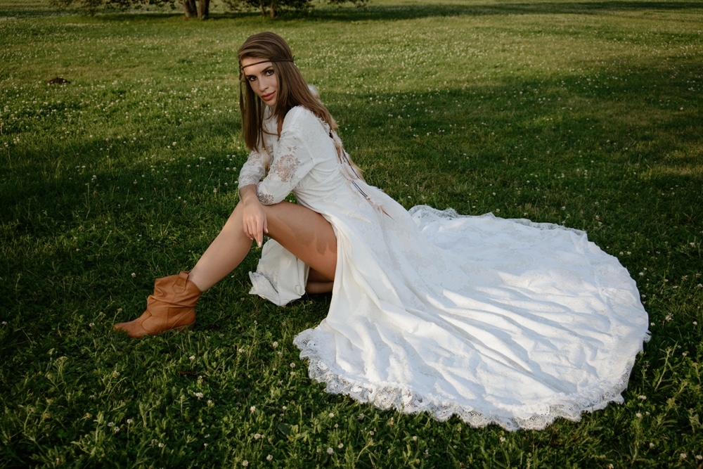 A young girl poses in a boho wedding dress, cowboy boots