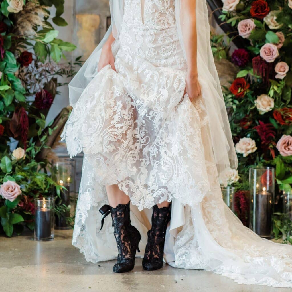 A view of a bride holding her white wedding dress with lace up grunge goth heeled boots