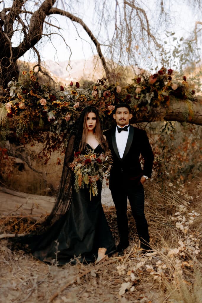 A view of a couple wearing black gothic themed dresses standing in the middle of a forest
