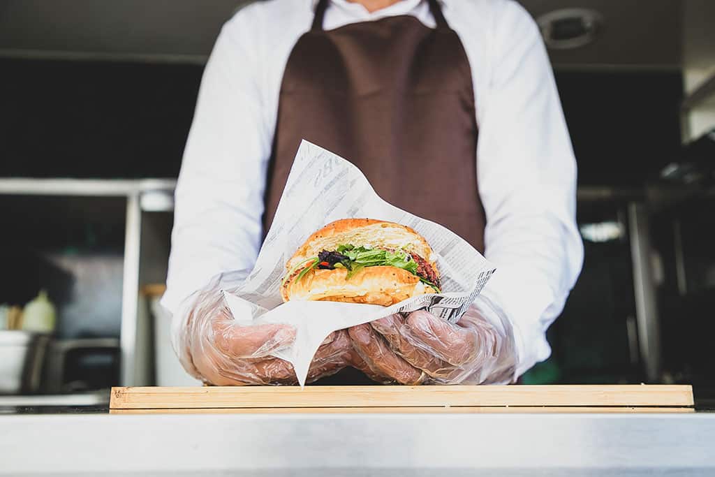 A view of a person serving a burger at a food truck wearing gloves