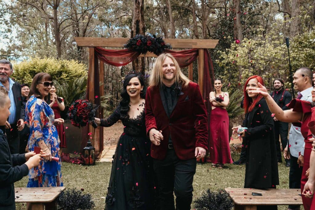 A view of couple walking down the aisle wearing a goth wedding attire with people looking at them