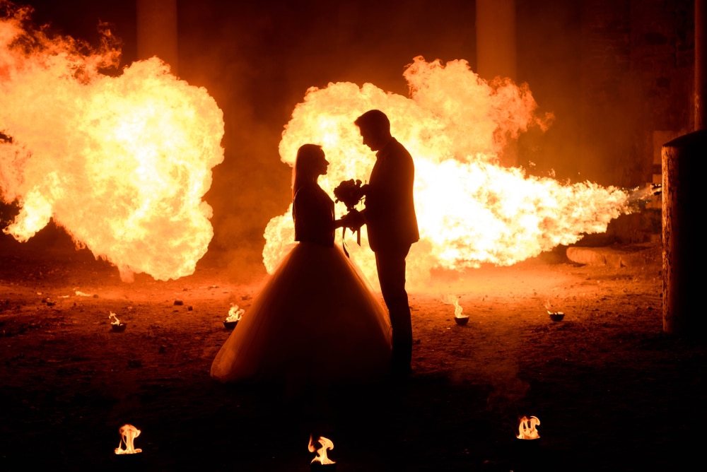 Wedding couple in medieval costumes with vampire style make-up standing in the dark against the backdrop of a big fire, Halloween theme