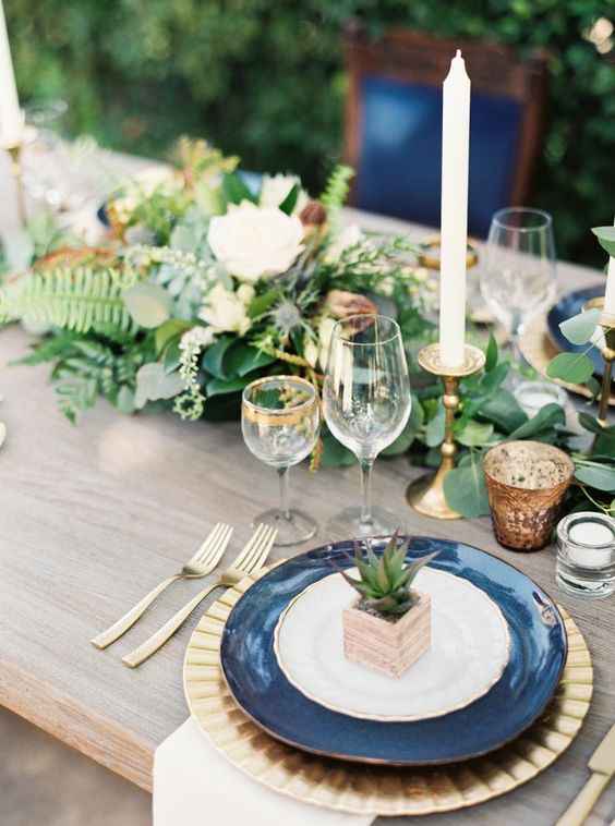 a wedding table along with the sage green flowers and navy blue plate with some other decorative items