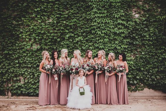 bridemaids wearing the dusty rose and sage green theme dresses along with bouquets in their hands