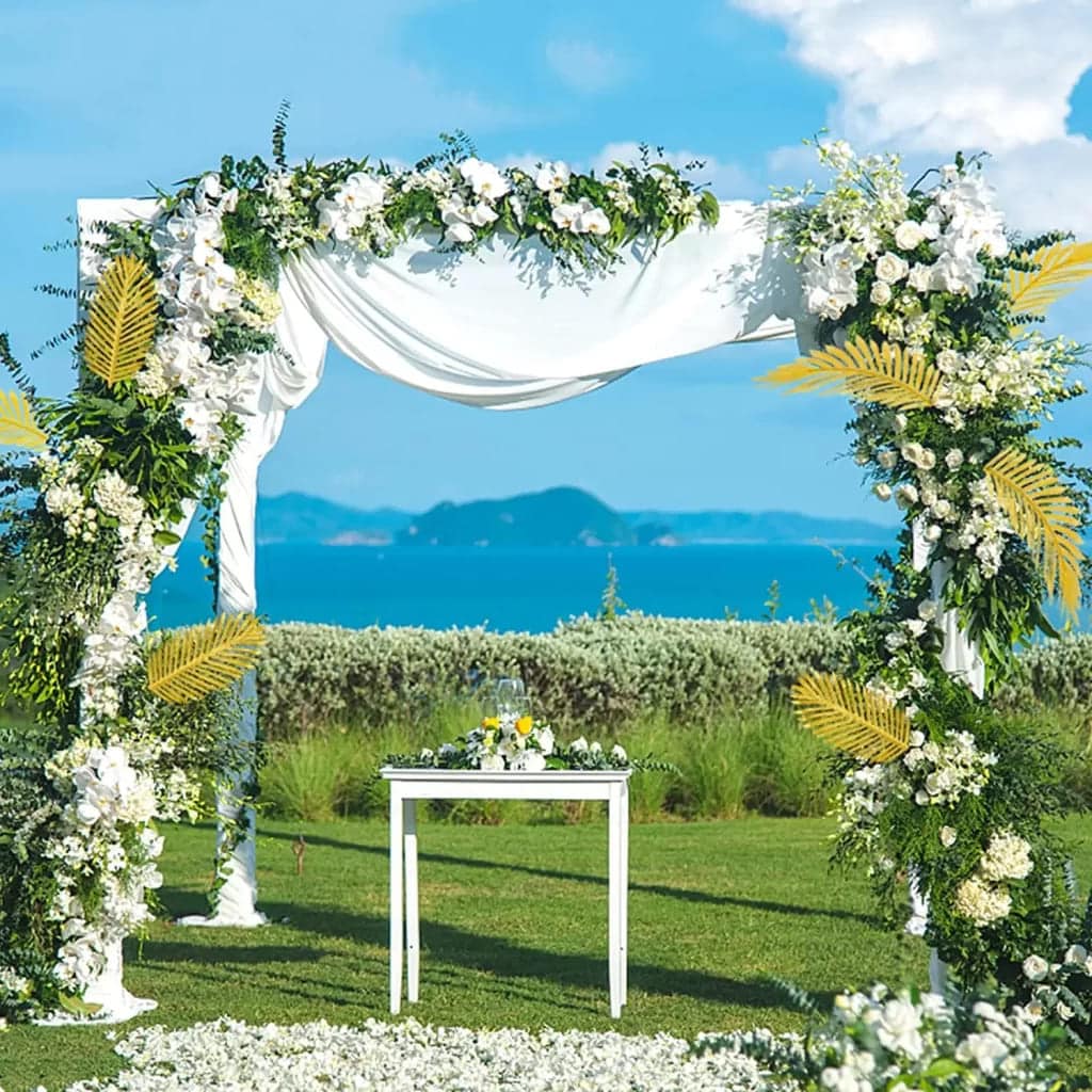 tropical palm wedding arch decorated with fake leaves abd flowers set up in an open ground