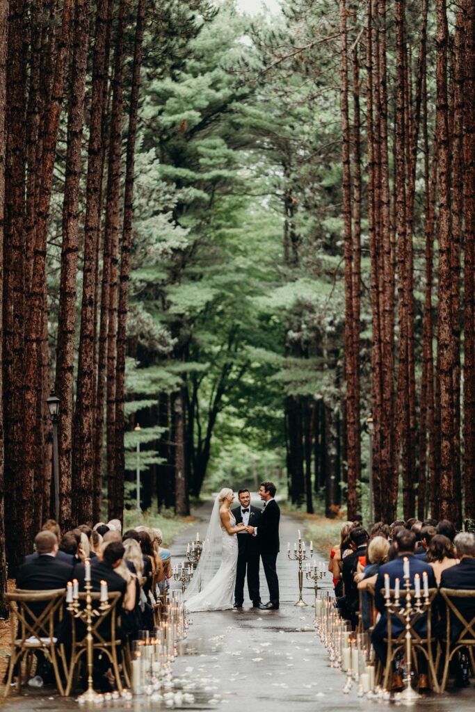 wedding aisle in woods with candles on the sides couple standing to exchange vows
