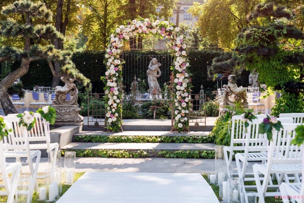 wedding setup in a gardeb with decorated arch white chairs and trees