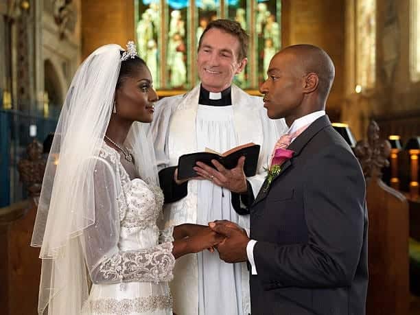 A view of a catholic bride and groom taking vows in a church with a father