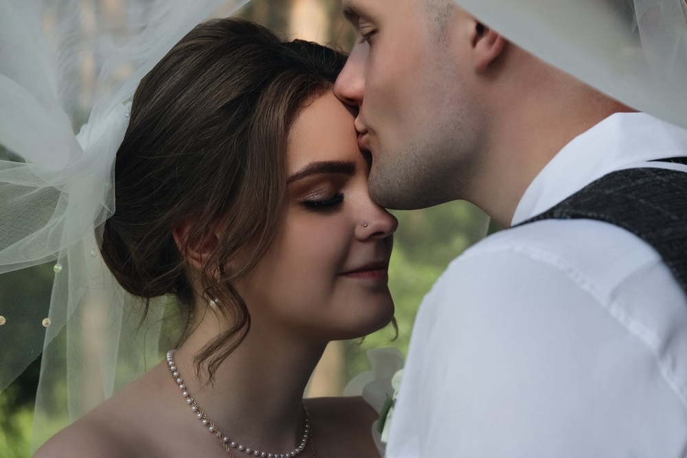 Portrait Of Happy Bride And Groom kissing the bride on forehead