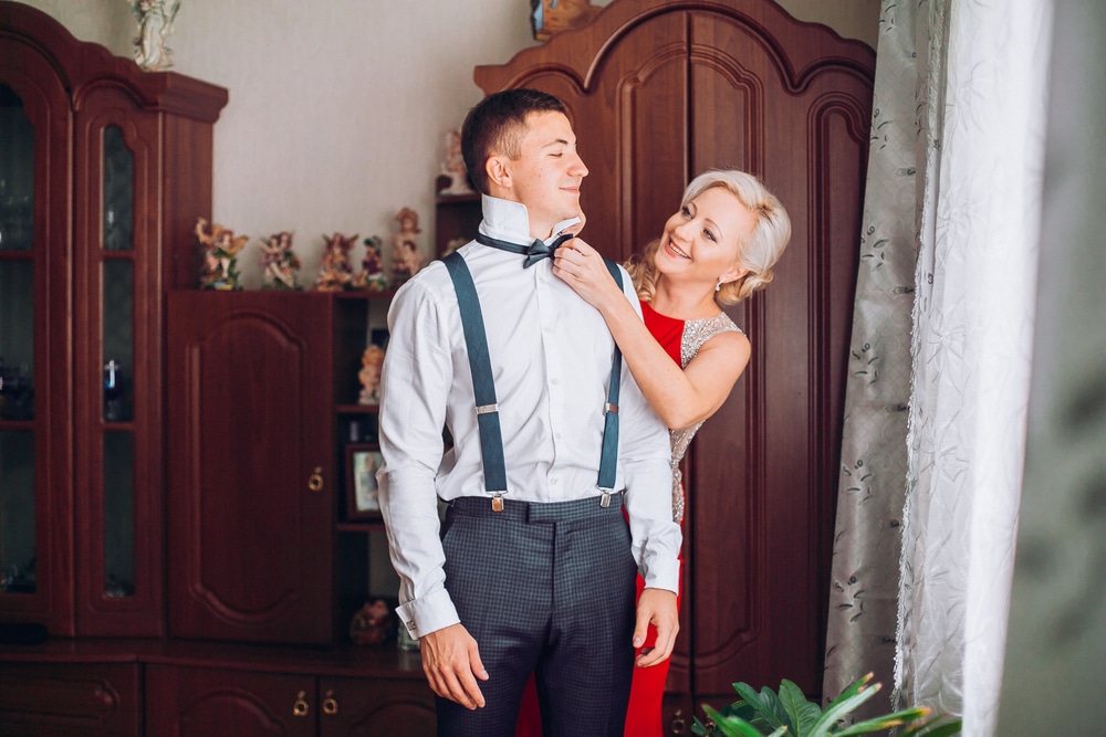 Mother is helping with a bow tie to her son before wedding ceremony