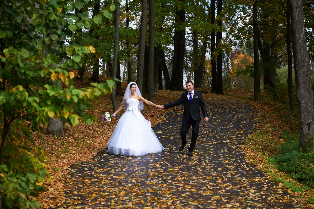 Happy Bride And Groom Walking In Yellow Autumn Park On