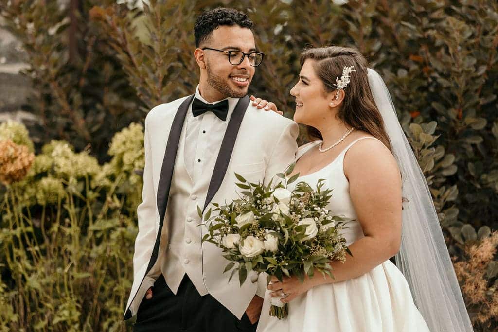 a wedding couple smiling at each other and bride having flowers in her hands