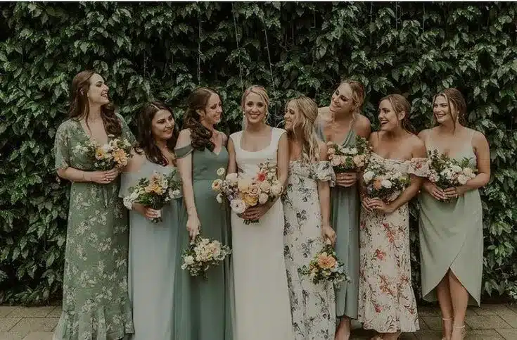 bride with bridesmaid wearing sage green dresses along with holding flowers in her hands