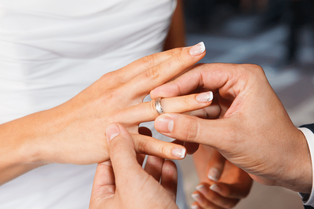 a man holding a women hand putting ring on her wedding finger 