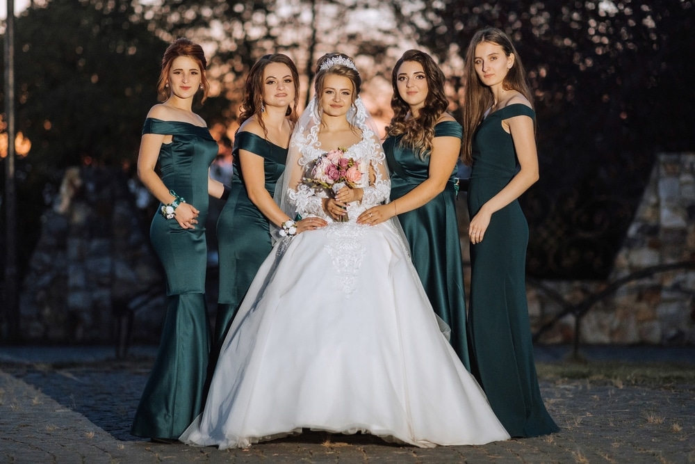 The bride is wearing a white dress and a veil. The bridesmaids are all wearing green dresses.