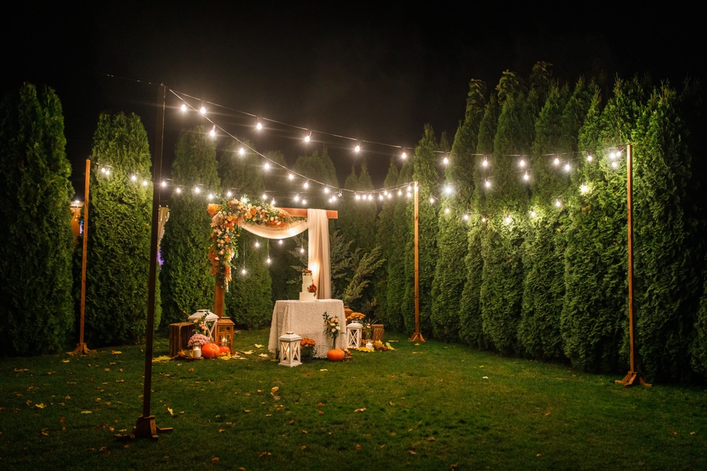 the arch is decorated with flowers, candles and garlands of light bulbs and there is a wedding cake on the table